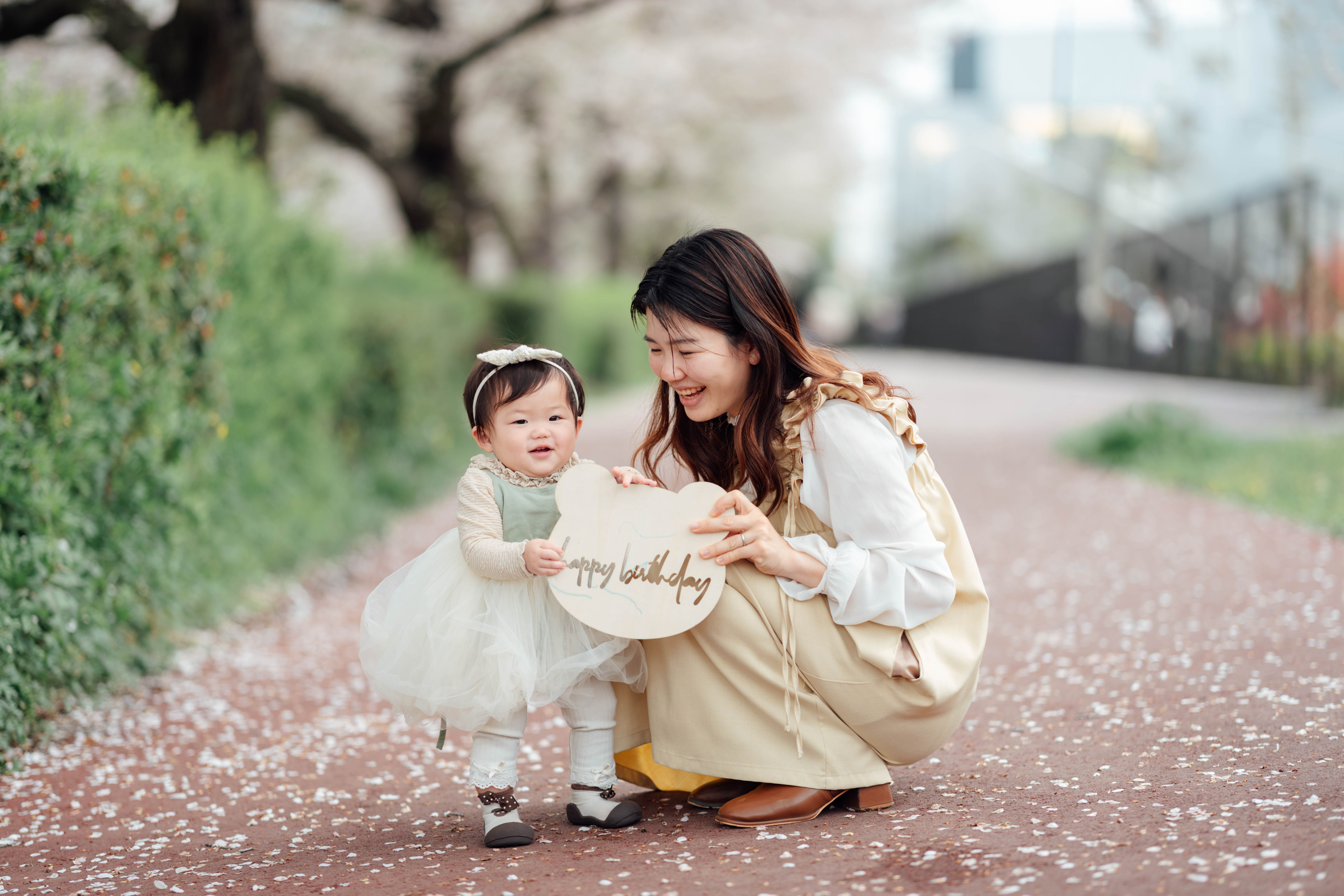 桜の下でバースデーボードを持つママと赤ちゃん